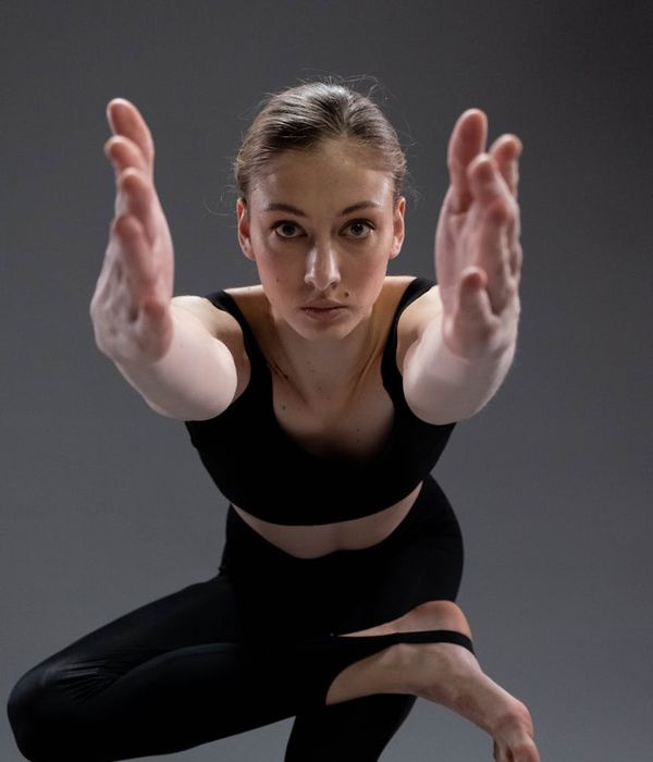 A young woman practicing gentle yoga stretches in a dark studio with warm lighting.